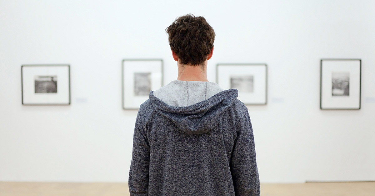 Back of man looking at wall of four pictures on a wall at a gallery